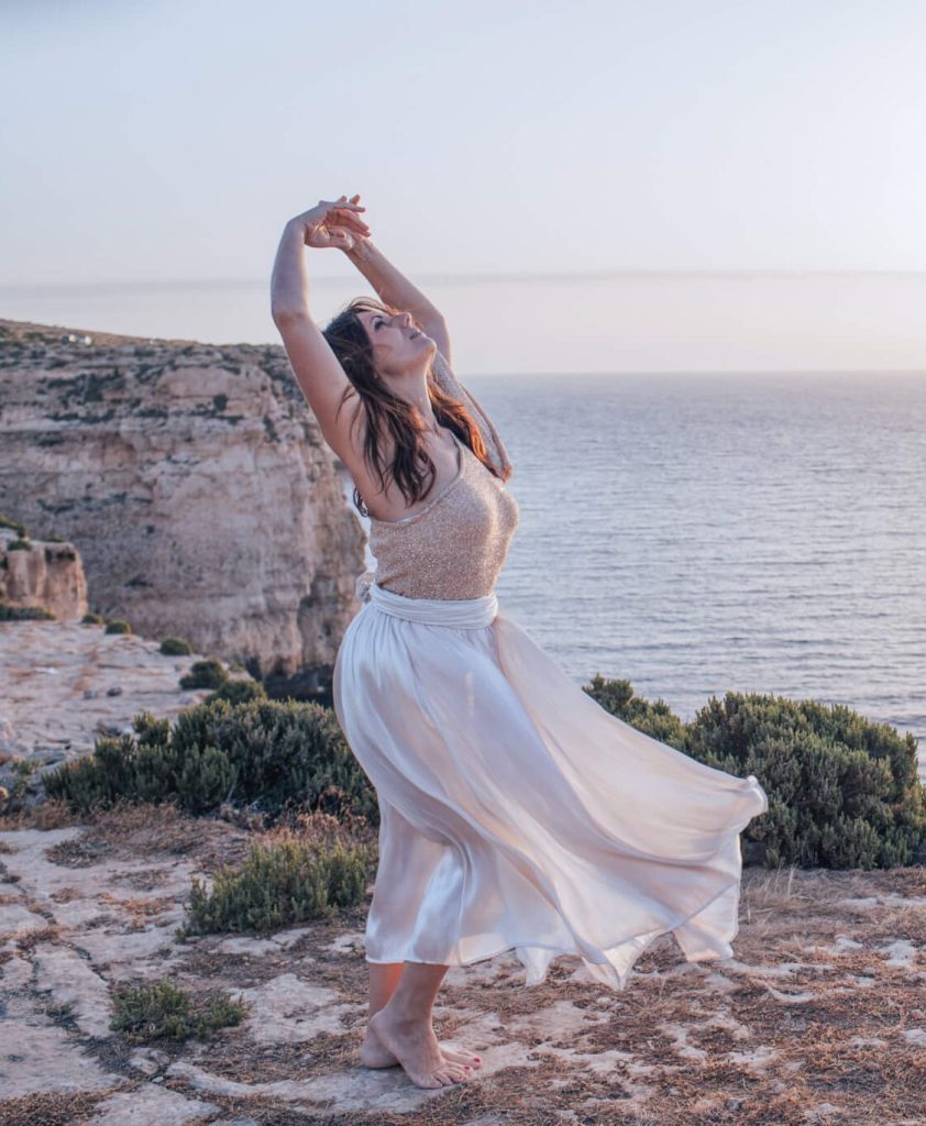 Woman practicing embodiment yoga on a cliff with the sea view behind